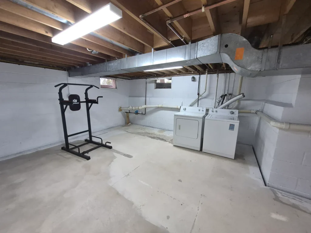 Exposed basement laundry near a concrete foundation corner in Bucks County, PA, showing plumbing lines in a residential utility space